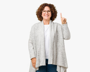 Beautiful middle ager senior woman wearing jacket and glasses over isolated background showing and pointing up with finger number one while smiling confident and happy.