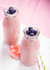 Pink milk shake in glass bottles topped with blueberries. Pink flowers and colorful straws.