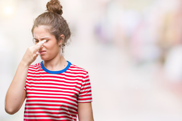 Beautiful brunette curly hair young girl wearing casual look over isolated background smelling something stinky and disgusting, intolerable smell, holding breath with fingers on nose