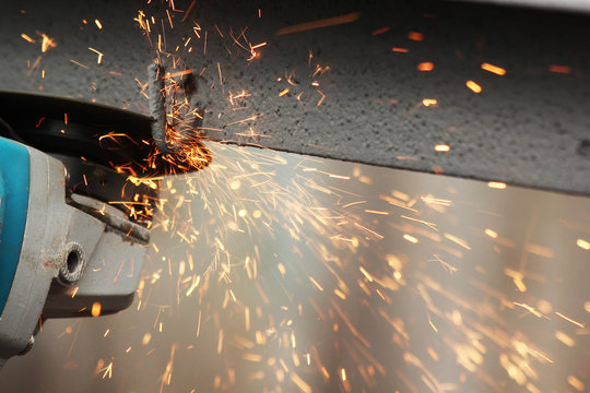 Industrial worker cutting metal with many sharp sparks working on angle grinder with circular blade