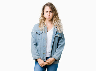 Beautiful young blonde woman wearing denim jacket over isolated background puffing cheeks with funny face. Mouth inflated with air, crazy expression.