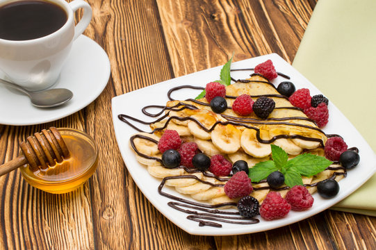 Homemade crepes served with chocolate cream, Banana, fresh blueberries, raspberries on a wooden background, pancakes.