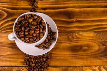 White cup filled with coffee beans on wooden table. Top view