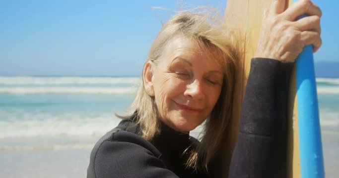 Front view of active senior Caucasian female surfer standing with surfboard on the beach 4k