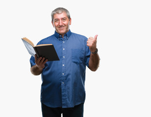 Handsome senior teacher man reading a book over isolated background pointing and showing with thumb up to the side with happy face smiling