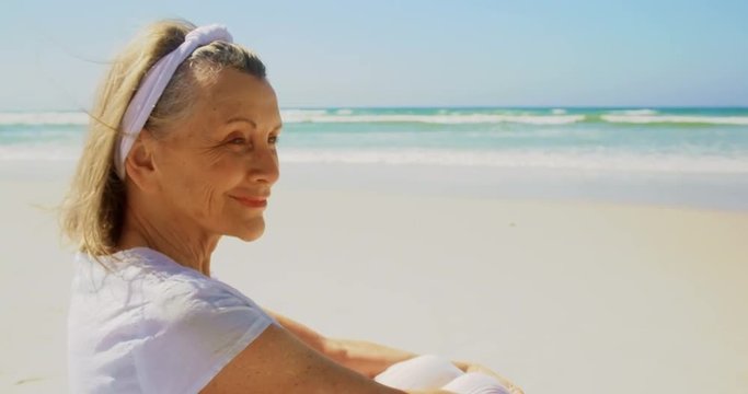 Side view of active senior Caucasian woman performing yoga on the beach 4k