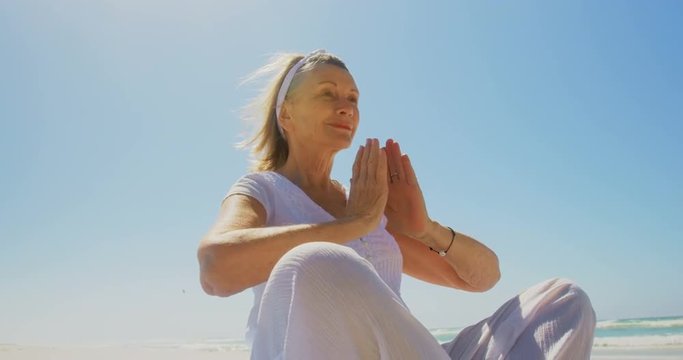 Low angle view of active senior Caucasian woman performing yoga on the beach 4k