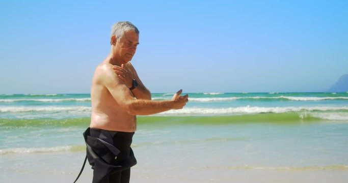 Side view of active senior Caucasian male surfer standing on the beach 4k