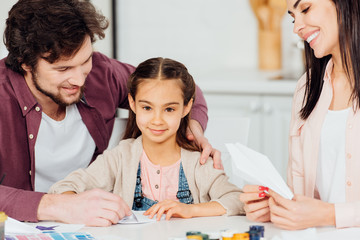 Fototapeta premium happy father smiling near cute daughter with paper plane at home