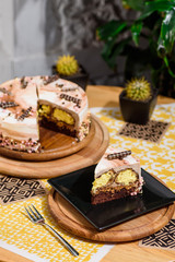 Beautiful chocolate layered cake with yellow filling and beautiful coffee glaze, decorated with tubules and pastry beads. Cake on a beautiful yellow background on a wooden table in the restaurant