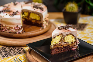 Beautiful chocolate layered cake with yellow filling and beautiful coffee glaze, decorated with tubules and pastry beads. Cake on a beautiful yellow background on a wooden table in the restaurant