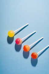 Lollipop candies in diagonal row on blue background top view with long shadow