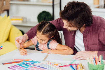 bearded father helping cute daughter drawing on paper