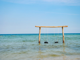 Beautiful sea landscape. High wooden swing decorated with colorful ribbons in a calm azure sea near the coastline.