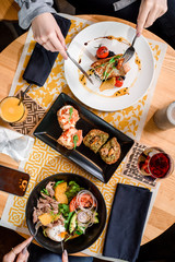 Lunch of two friends in a restaurant with salad with avocado, tomatoes, poached egg, beef, orange, arugula and roasted salmon fillet and risotto with cuttlefish. Close up. Top view.