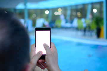 Man pointing finger on screen smartphone on background in night atmospheric Swimming pool using in male hands and texting mobile phone. Spa wellness center. Technology and phone addiction concept