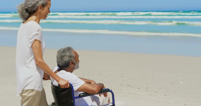 Side view of active senior African American woman with disabled senior man on beach in sunshine 4k
