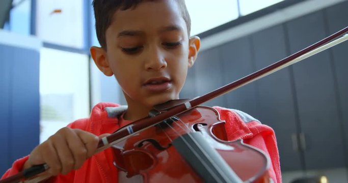 Front view of attentive Asian schoolboy playing violin in classroom at school 4k