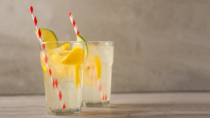 two glass of lemonade with lemons and lime and straw, on a dark background, with space, a cool drink and summer mood