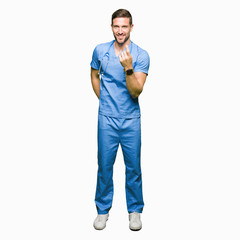 Fototapeta premium Handsome doctor man wearing medical uniform over isolated background Beckoning come here gesture with hand inviting happy and smiling