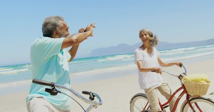 Side view of active senior African American man taking photo of woman with mobile phone at beach 4k