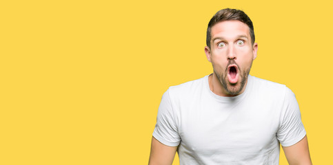 Handsome man wearing casual white t-shirt afraid and shocked with surprise expression, fear and...