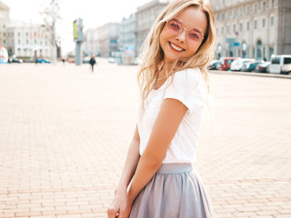 Fototapeta premium Portrait of beautiful smiling blond model dressed in summer hipster clothes. Trendy girl posing in the street background in round sunglasses. Funny and positive woman having fun