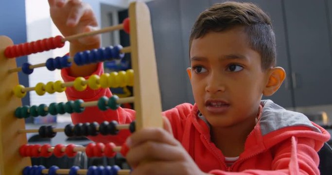 Front view of Asian schoolboy solving math problem with abacus at desk in a classroom at school 4k