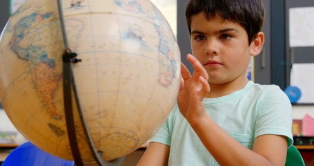 Front view of Caucasian schoolboy studying globe at desk in classroom at school 4k