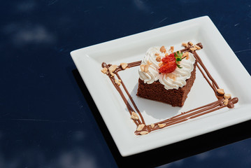 Beautiful chocolate cake with cream and strawberries on a white each-square plate on a glass table in a restaurant. Close-up. Spread