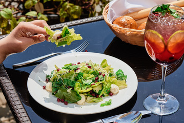 Girl eating fresh vegan salad with spinach, lettuce, pomegranate, wheat sprouts on a white plate on a dark glass table in a restaurant. Breakfast on the terrace