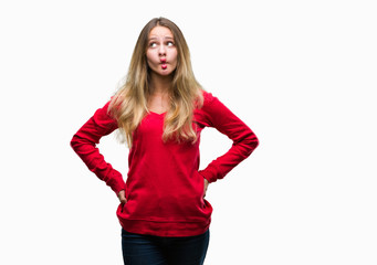 Young beautiful blonde woman wearing red sweater over isolated background making fish face with lips, crazy and comical gesture. Funny expression.