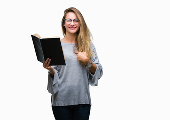 Young beautiful blonde woman reading a book over isolated background with surprise face pointing finger to himself