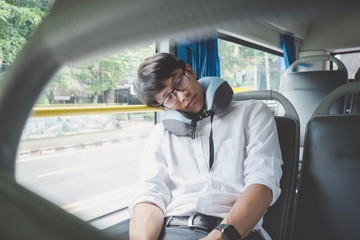 Fototapeta na wymiar Young Asian man traveler sitting on a bus and sleeping with pillow, transport, tourism and road trip concept