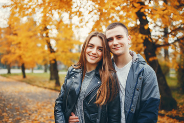 Cute couple walking in a autumn park. Boy in a black jacket. Girl in a gray dress