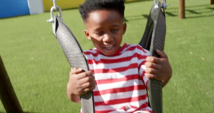 Front view of African American schoolboy playing on a swing in school playground 4k