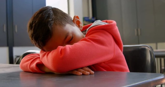 Front view of Asian schoolboy sleeping over the desk in classroom at school 4k
