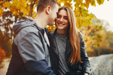 Fototapeta premium Cute couple sitting in a autumn park. Boy in a black jacket. Girl in a gray dress