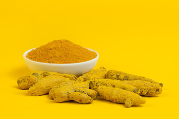 Turmeric root and turmeric powder on yellow background. Free space for text.