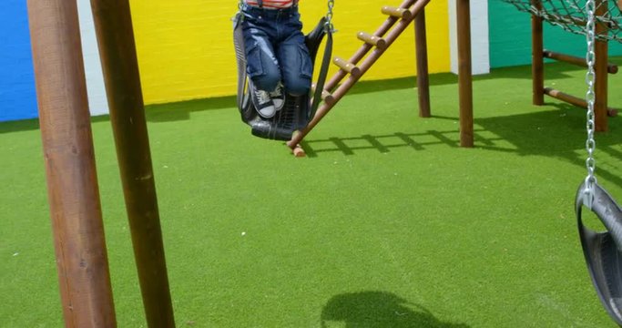 Front view of mixed-race schoolgirl playing on a swing at school playground 4k