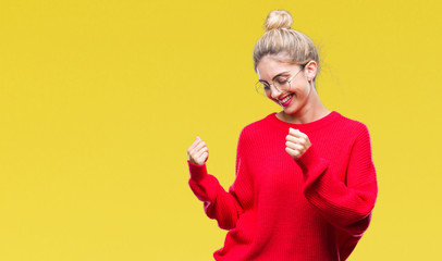 Young beautiful blonde woman wearing red sweater and glasses over isolated background very happy and excited doing winner gesture with arms raised, smiling and screaming for success