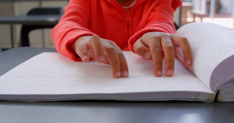 Mid section of blind Asian schoolboy hand reading a braille book in classroom at school 4k - Powered by Adobe