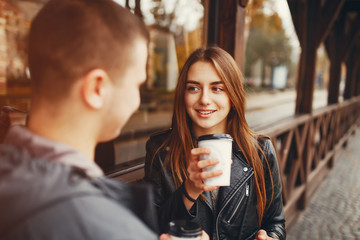 Cute couple standing near brown building. Boy and girl have fun in a autumn city. Couple drinking a coffee