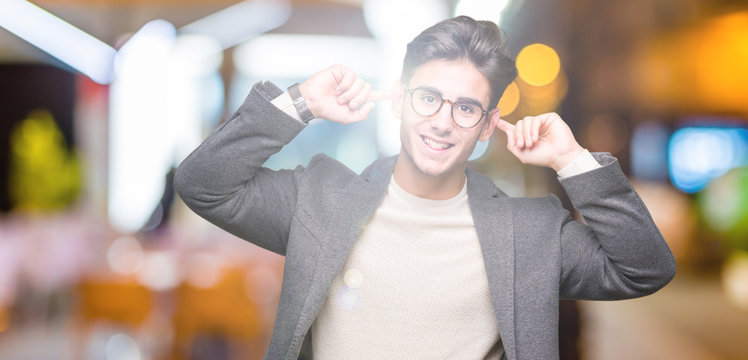 Young business man wearing glasses over isolated background Smiling pulling ears with fingers, funny gesture. Audition problem