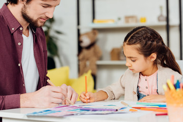 Naklejka premium selective focus of cute daughter drawing with handsome father