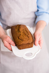 Women's hands holding freshly baked cake with grains and seeds. Homemade cakes are served on a ceramic board.