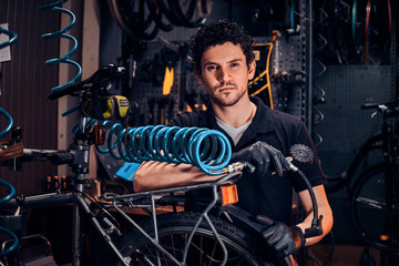 Fototapeta na wymiar Handsome talented master is fixing bicycle at his own workshop using pneumatic tool.