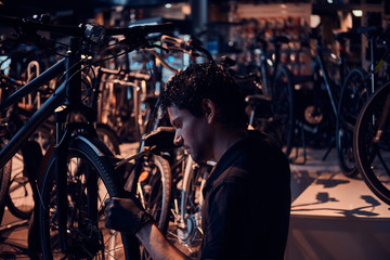 Fototapeta na wymiar Diligent attractive mechanic is repairing customer's bicycle at workplace.