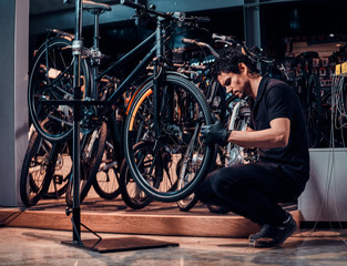 Expirienced young master is repairing customer's bicycle at workplace.