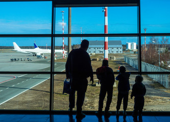 father and sons standing in the airport near big window looking on the airplane wearing casual clothes